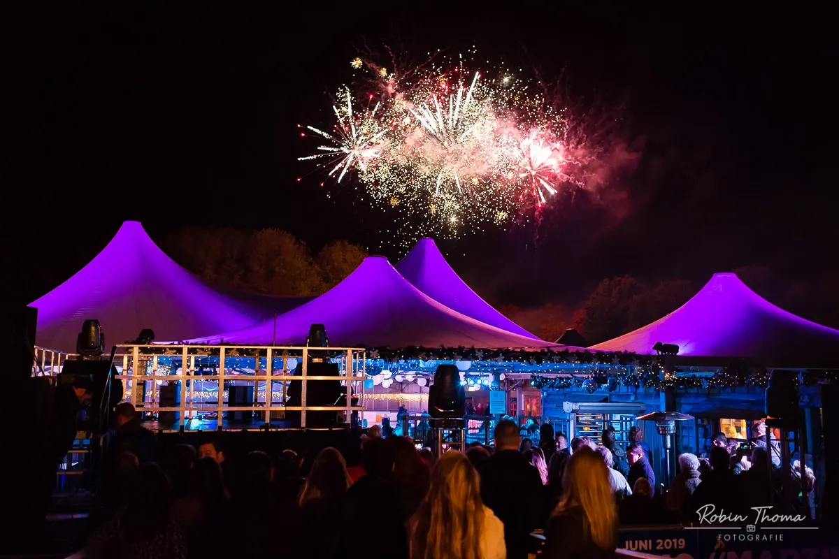 The purple-lit tents of the Ice Paradise rink at night in Leidschendam, with fireworks in the sky above. — Ice Paradise