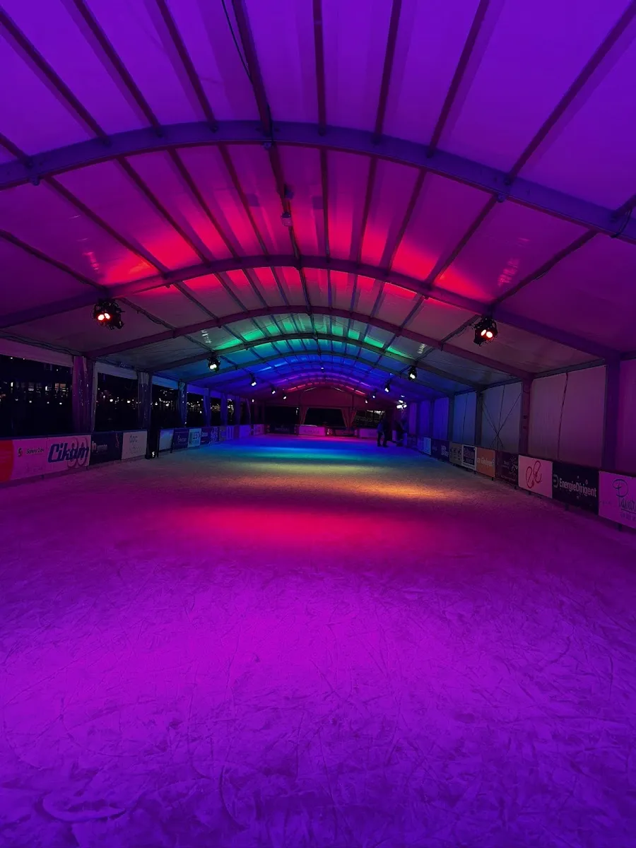 The long, empty ice rink inside the tent hall, lit in violet, red and green under the arched canopy ribs. — Ice Paradise