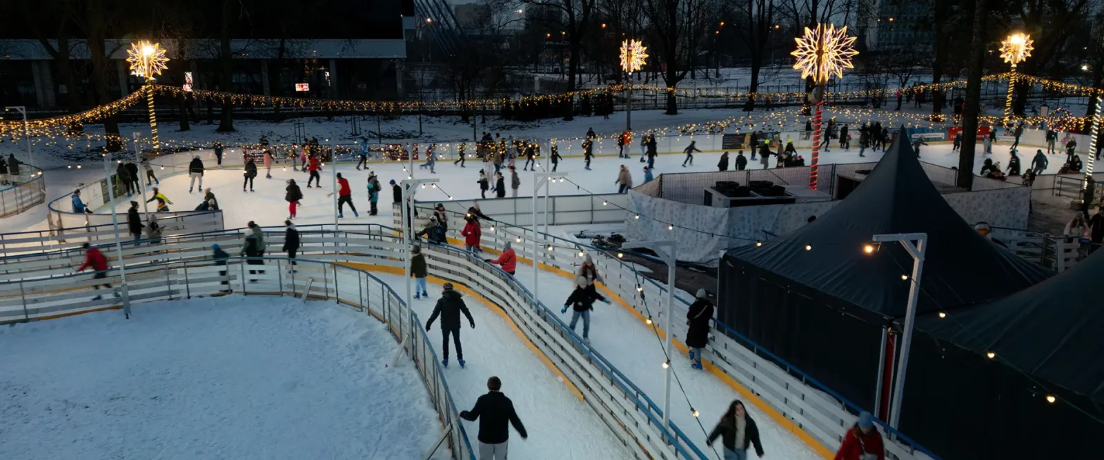 Skaters circling the lit ice of the Ice Park rink in Park Jordana at night, seen from above. — Ice Park Kraków (Park Jordana)