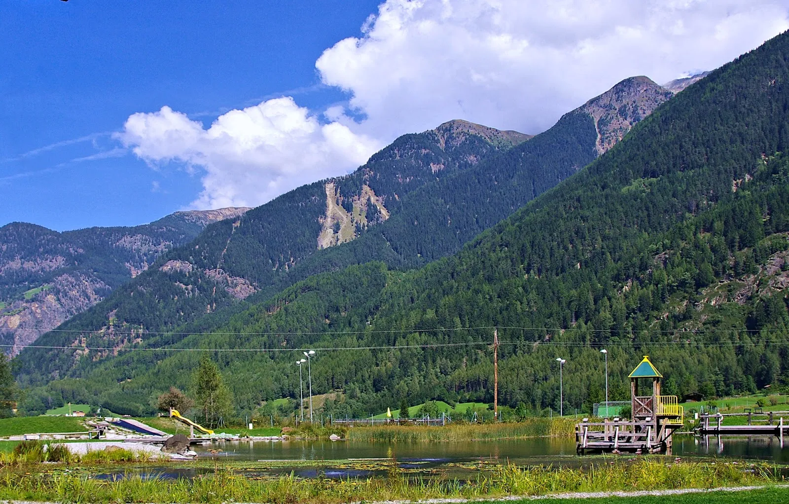 Der Naturbadesee Umhausen im Sommer, der See, um den im Winter der Eisweg des Ice Parks verläuft – Ice Park Umhausen