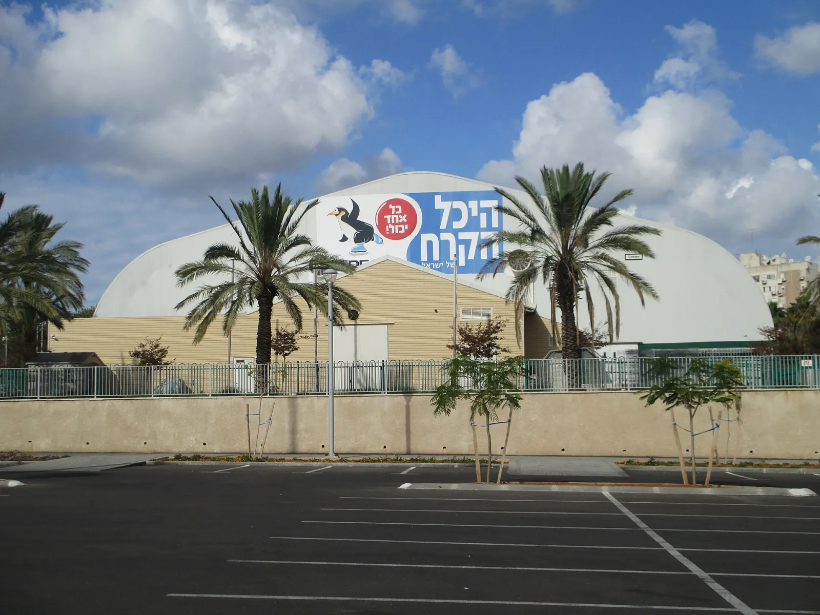 The dome of the Ice Peaks rink in Peres Park, Holon, seen across its car park, with the Hebrew sign on the wall — Ice Peaks Holon