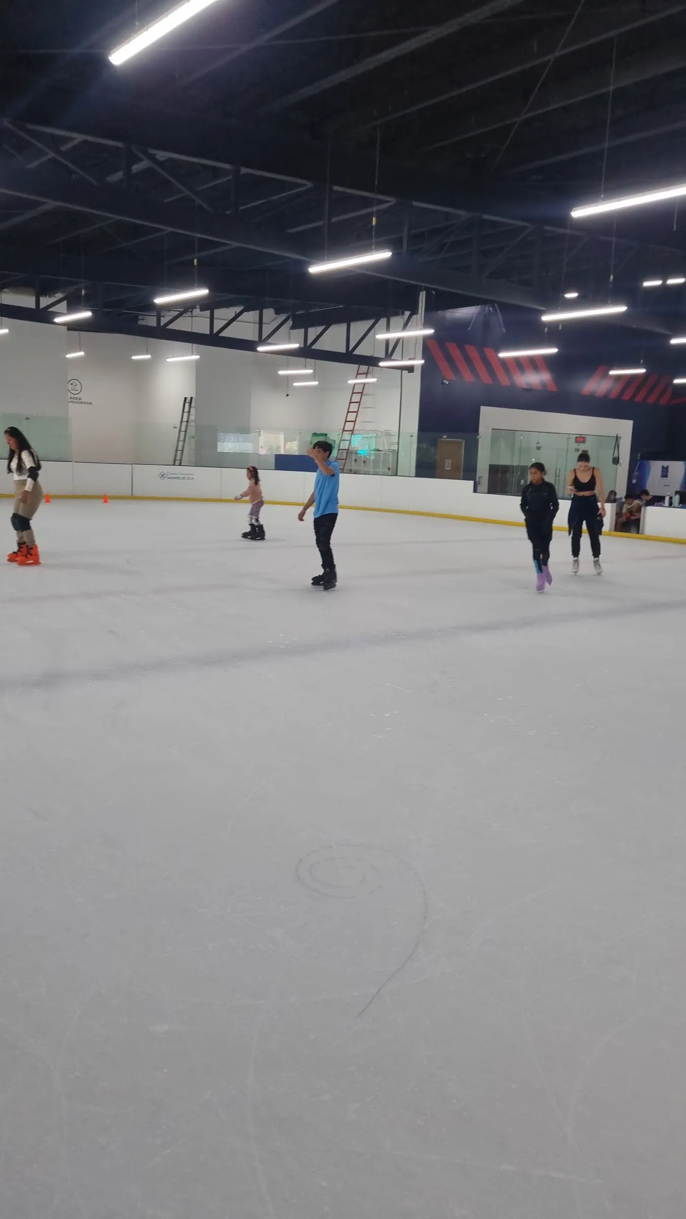 El hielo de Ice Place en Cuernavaca con unos cuantos patinadores cerca de las vallas del fondo, bajo el techo negro con hileras de luces. — Ice Place Cuernavaca