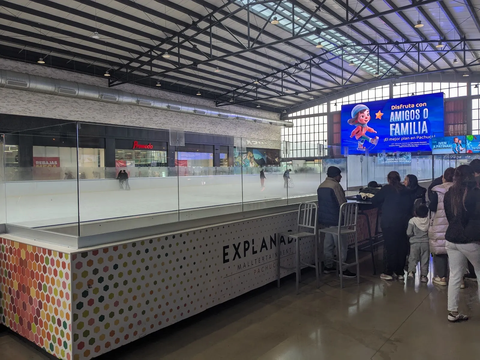 The glass-walled rink inside Explanada Pachuca, with skaters on the ice and the mall hall behind it — Ice Place Pachuca