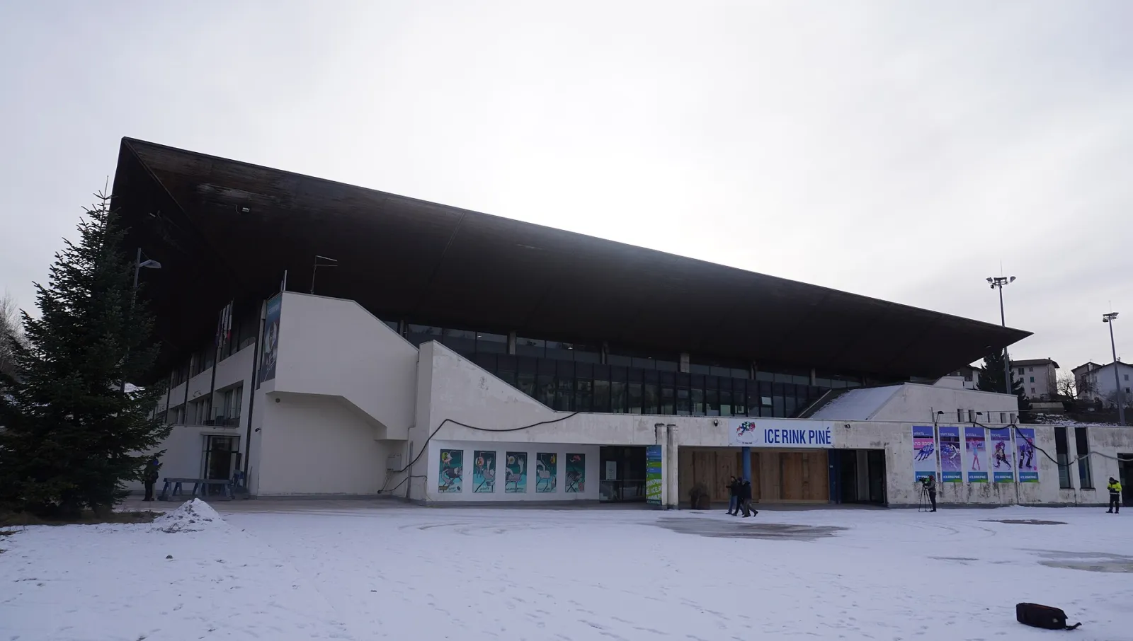 The sports hall of Ice Rink Piné with its sloping dark roof and the ticket entrance with the Ice Rink Piné sign, on a snowy winter day. – Ice Rink Piné