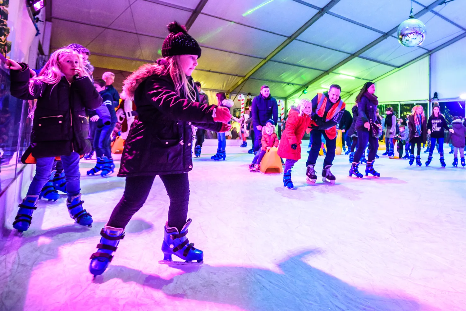 A crowded public session on the lit ice under the marquee at Ice Skating in the Park, Bognor Regis, with skating aids and coloured lighting — Ice Skating in the Park (Bognor Regis)