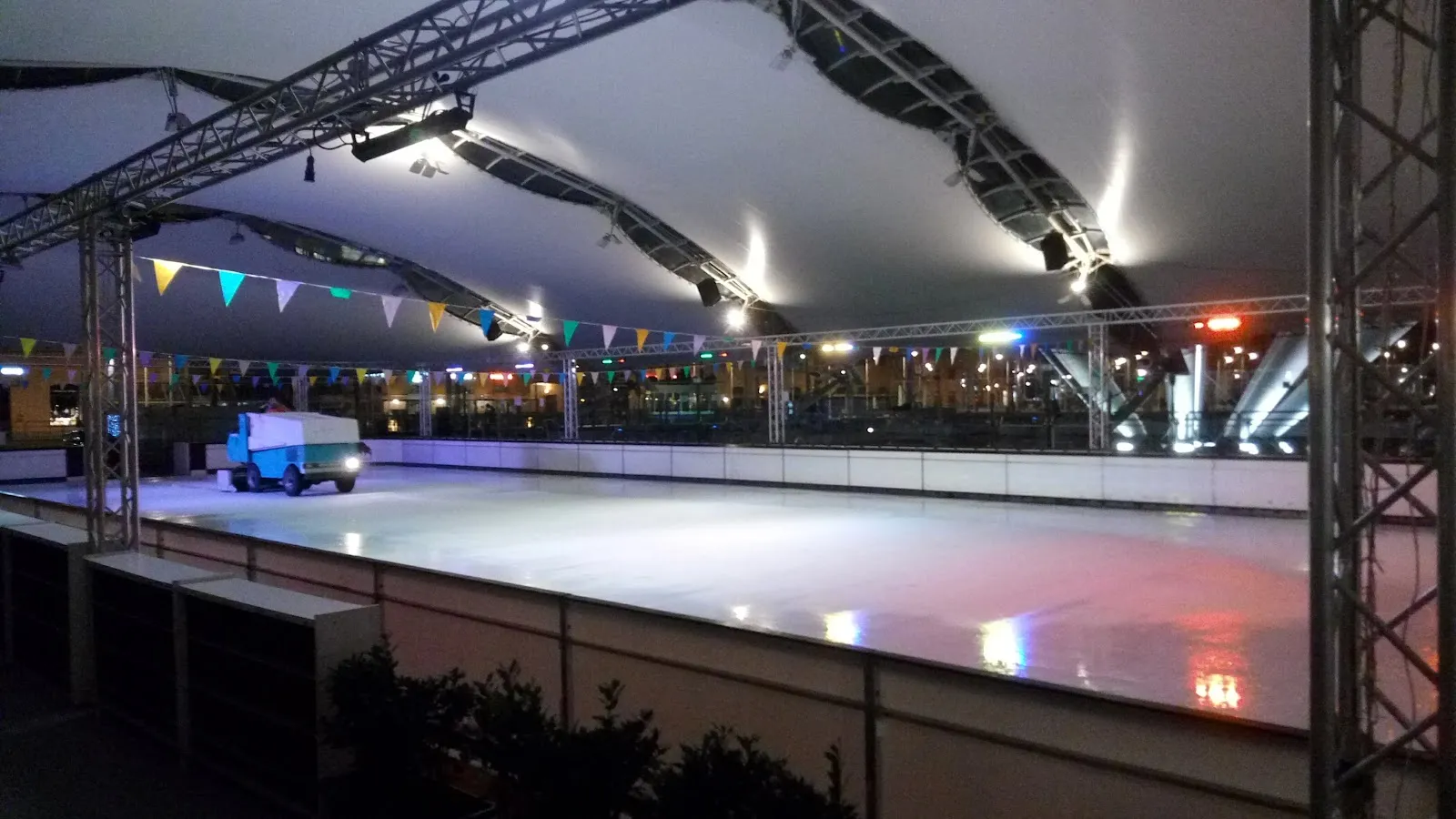 Il ghiaccio vuoto di notte sotto il tendone bianco, con una rasaghiaccio all’estremità opposta e festoni lungo le balaustre. – Ice Skating Rink Genova (Porto Antico)