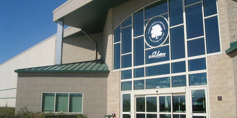 The arena's glass entrance tower with the Ice Valley and Kankakee Valley Park District emblems, tan block walls and a green metal canopy under a blue sky. — Ice Valley Centre