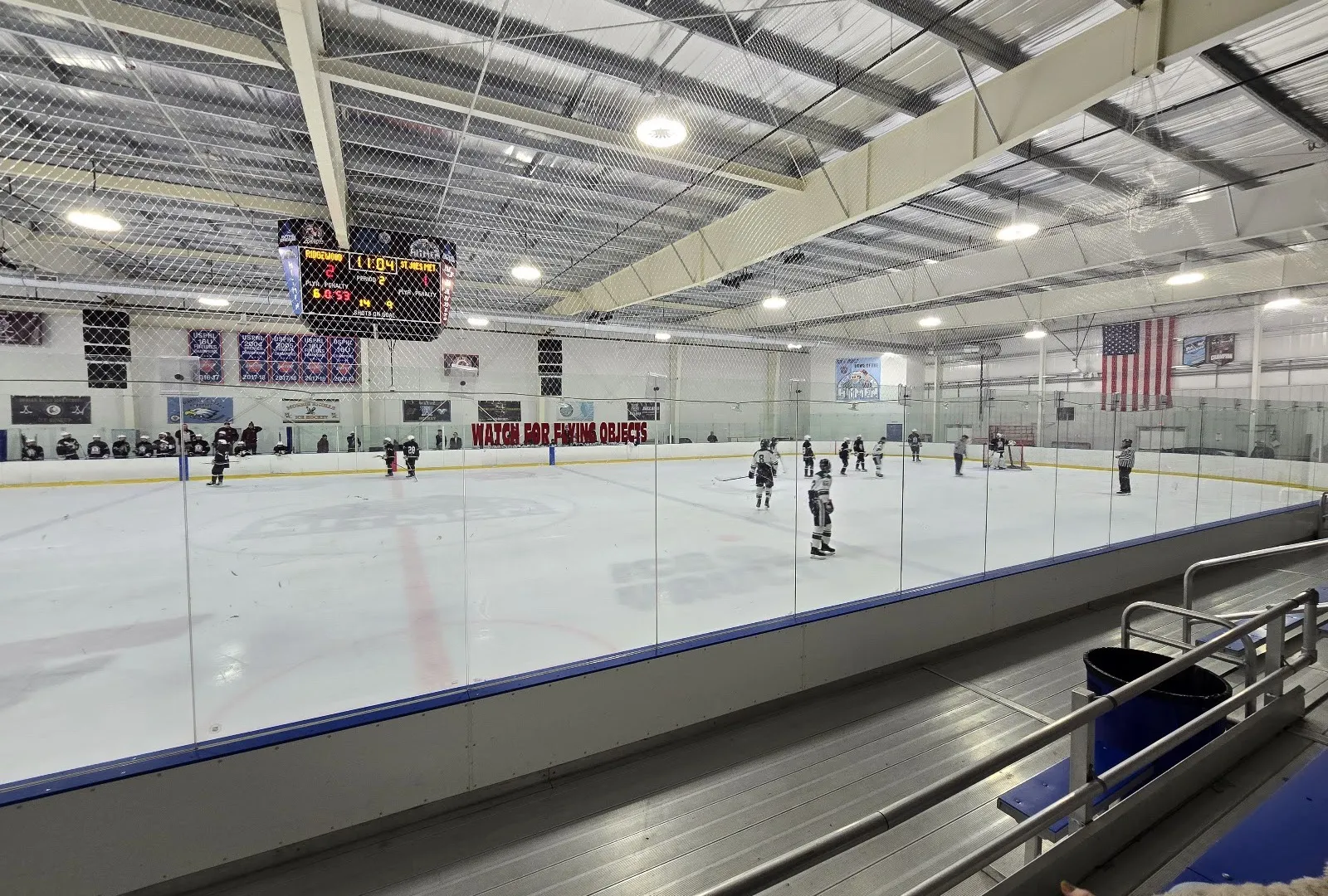 A rink at Ice Vault Arena from the stands during a game, the scoreboard and banners hanging over the far end — Ice Vault Arena