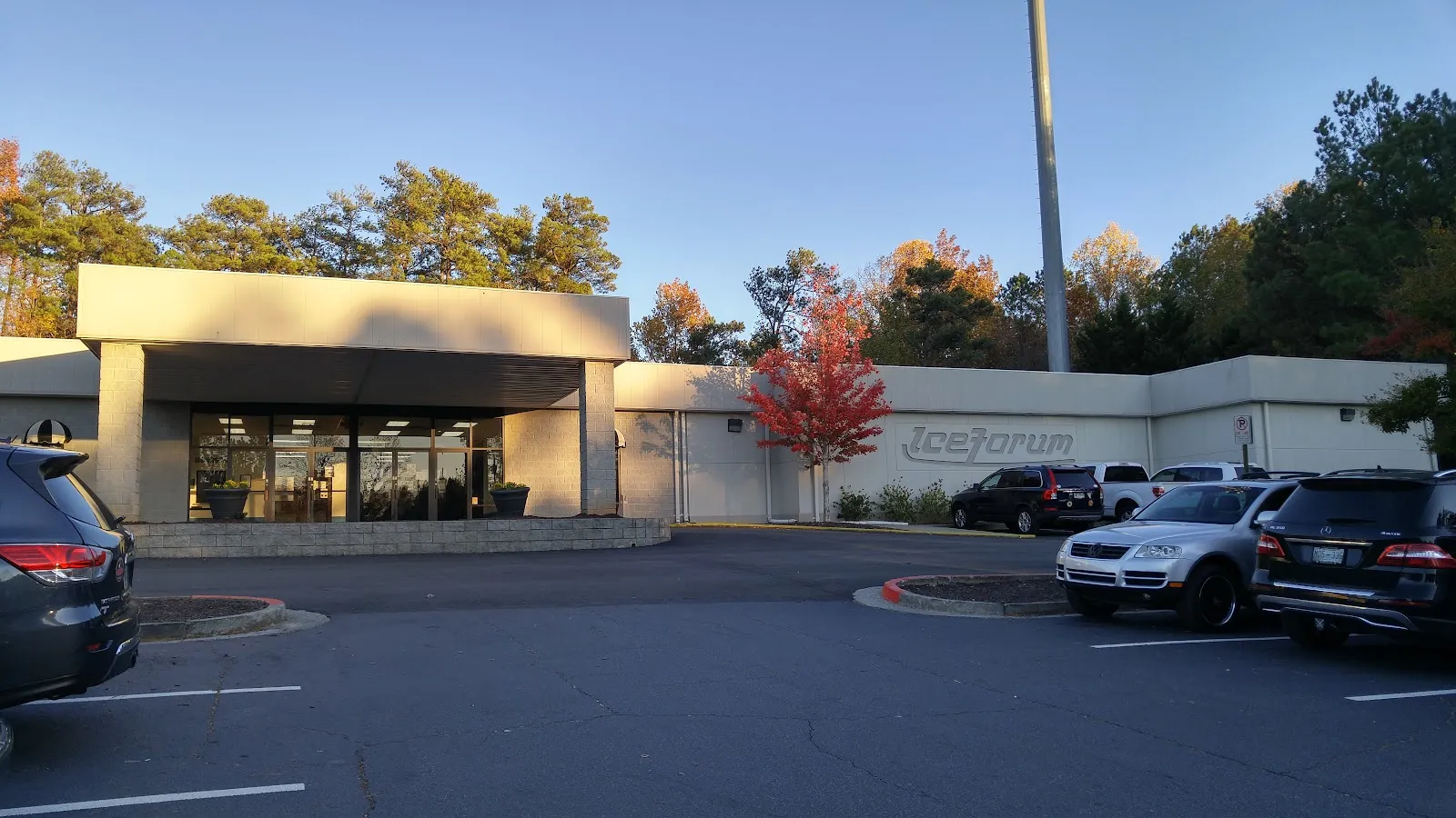 El edificio bajo y blanco de IceForum con su entrada de vidrio bajo una marquesina plana, visto desde el otro lado del estacionamiento con la luz de la mañana temprano. — Atlanta IceForum