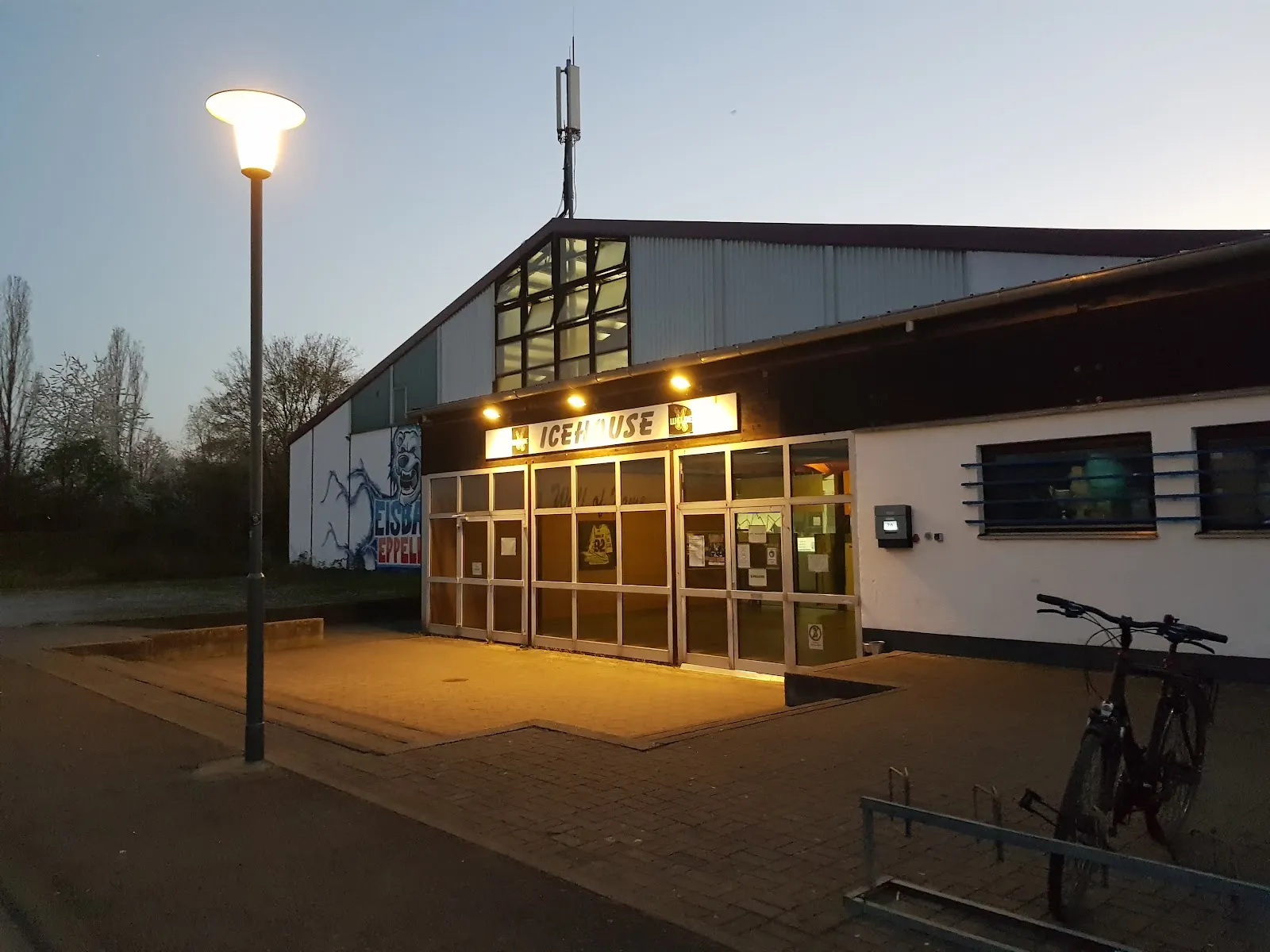 The lit Icehouse entrance in Eppelheim at dusk, with the name above the glazed doors and a street lamp in front — Icehouse Eppelheim