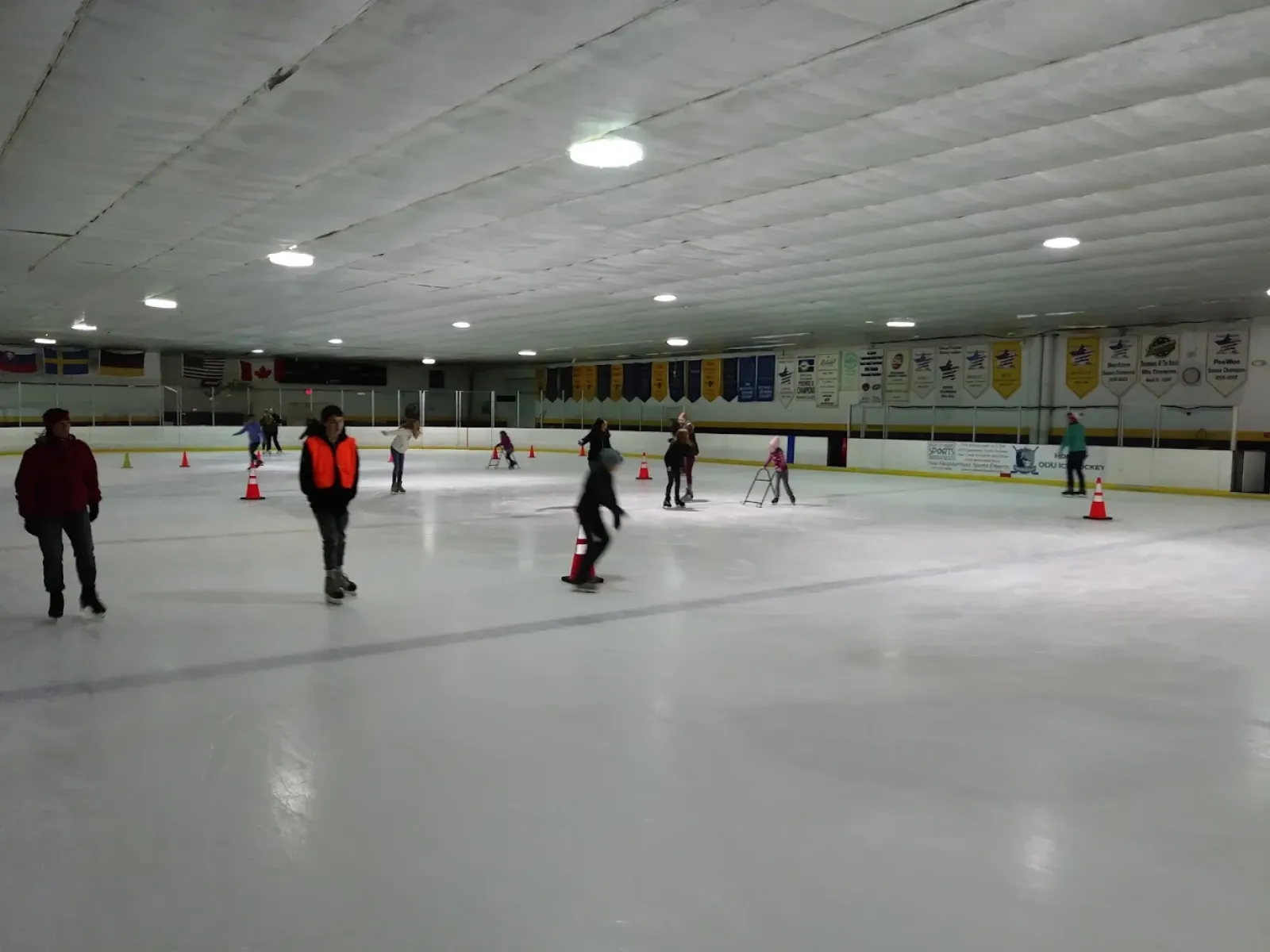 Amplia vista de la pista durante un patinaje público, con mantas de campeonato y banderas nacionales colgadas a lo largo de la pared del fondo. — Iceland Family Skating Center