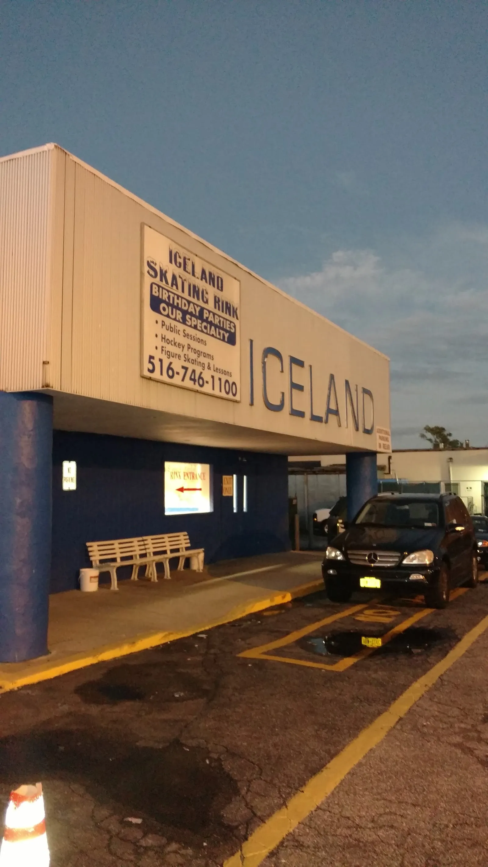 La fachada de Iceland al anochecer, con ICELAND en letras grandes y un letrero de Iceland Skating Rink en el alero, sobre columnas azules y una banca. — Iceland Long Island