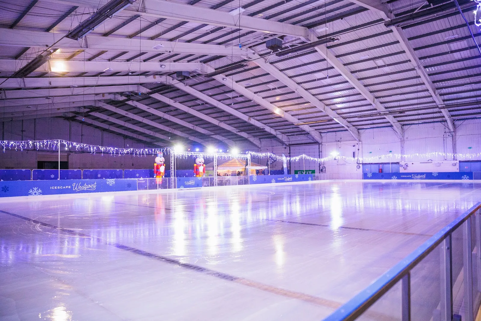 The empty temporary ice sheet inside Westpoint Arena in Exeter, lit in purple under the roof trusses with festive lights along the boards — Icescape Westpoint