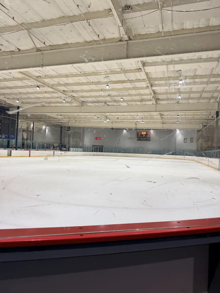 Empty full ice sheet at Icetown Riverside seen through the glass, scoreboard reading 20:00 on the far wall, net visible at one end, insulated metal ceiling overhead. — Icetown Riverside