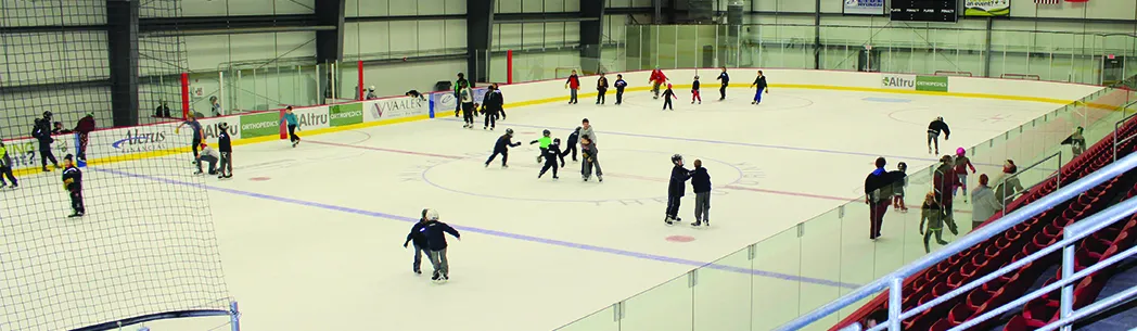 Patinadores en una de las pistas de la arena del Grand Forks Park District, en la foto de encabezado de renta de la arena en sus páginas de instalaciones (las bardas llevan los patrocinadores de ICON). — ICON Sports Center