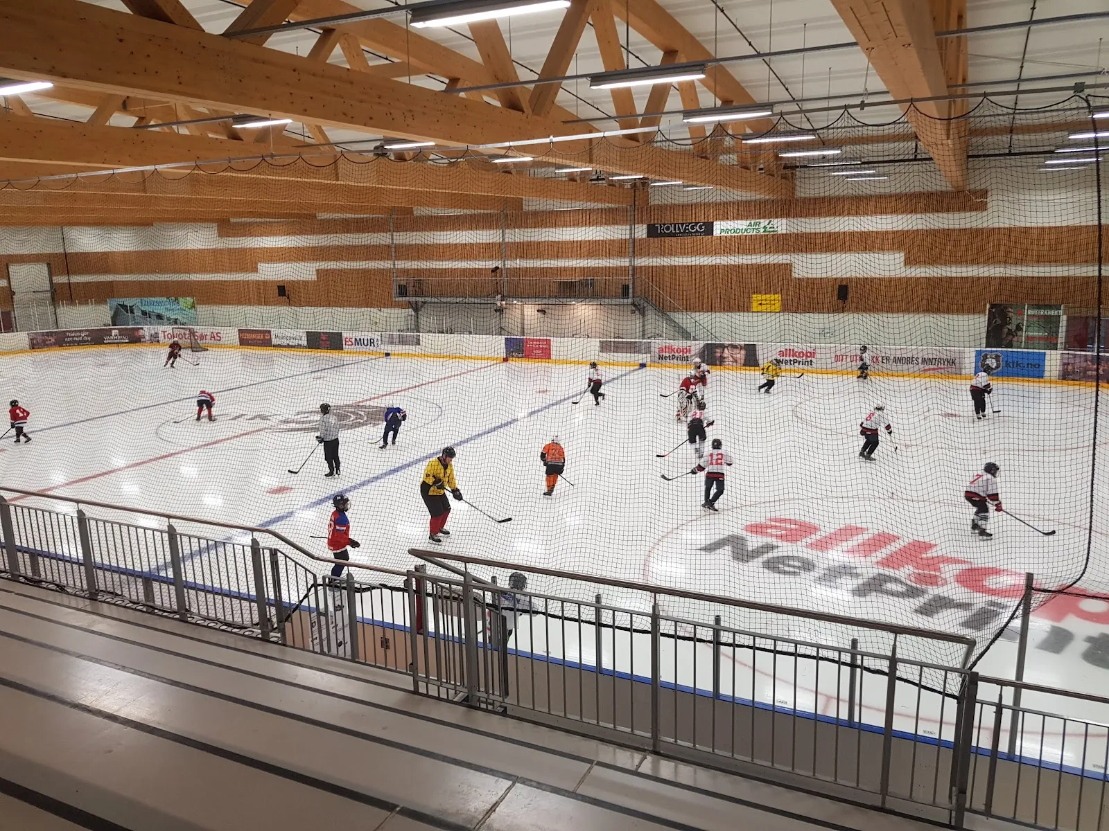 A wide view of the ice sheet in Idda Arena under a timber roof, with a few skaters on the ice and spectator rails in front. — Idda Arena (ishall)