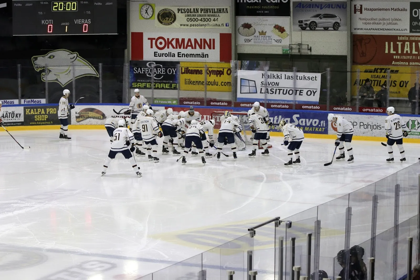 Two teams lined up on the ice of Iisalmi ice rink before a game, seen from the rink-side with the boards and stands behind. — Iisalmen jäähalli