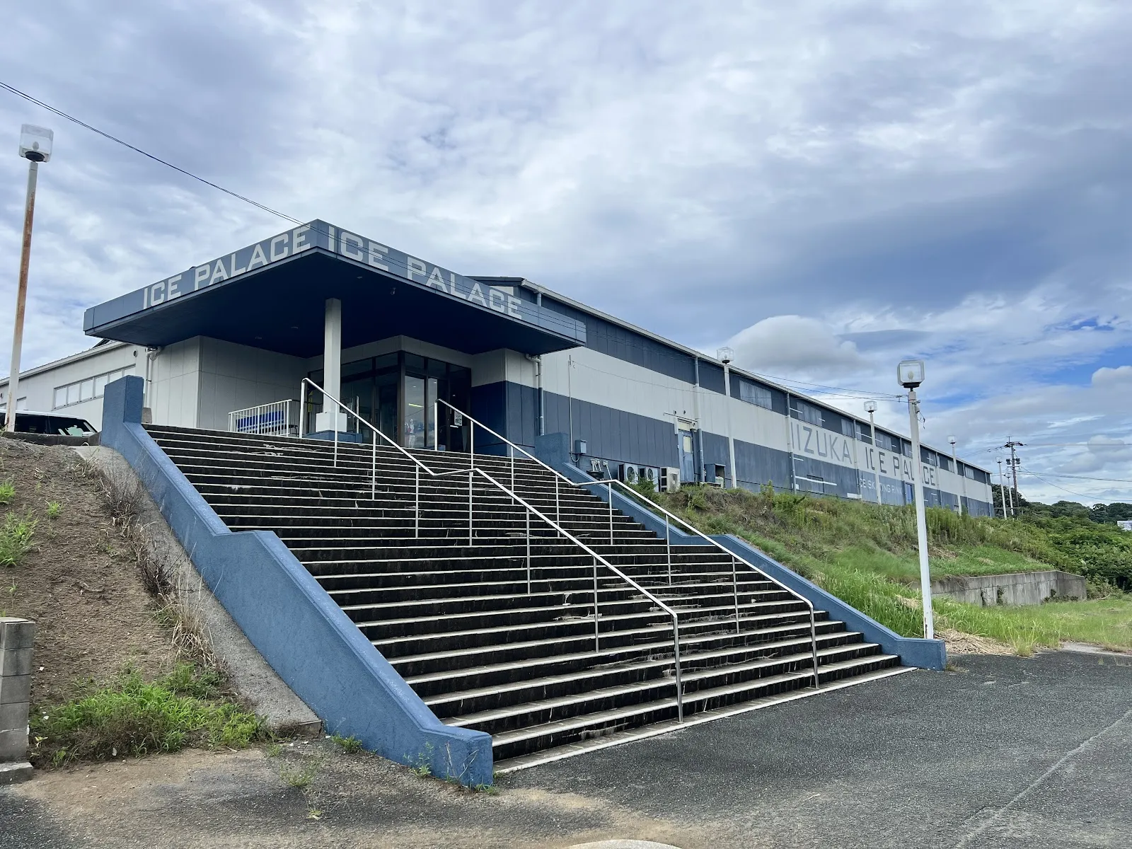 The long metal-clad Iizuka Ice Palace building with its Ice Palace sign over the entrance and a wide concrete staircase leading up to it. — Iizuka Ice Palace