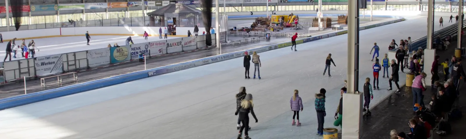 Skaters in a public session on the 400 m track and the 30x60 m rink inside the hall at IJsbaan De Westfries in Hoorn, seen from the stands — IJsbaan De Westfries