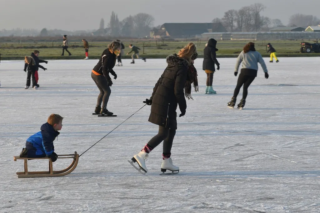Skaters, one pulling a child on a wooden sledge, on the pale natural ice of the HWZ rink with farmland and trees behind. — IJsbaan HWZ