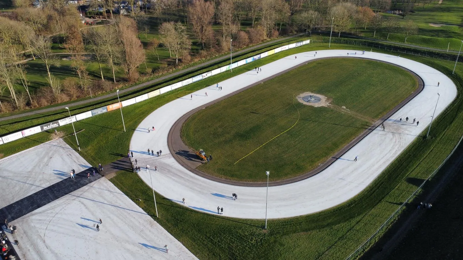 An aerial view of the oval natural-ice track in Kerkdriel on its Christmas 2025 opening day, with skaters spread along the ice and the grass infield in the middle. — IJsbaan Kerkdriel (de Griend)