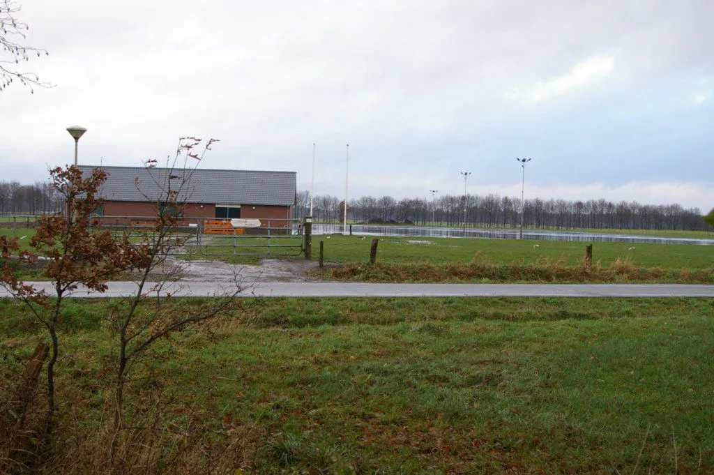 Brick clubhouse seen across the grass with the rink field behind it. — IJsbaan Ruurlo