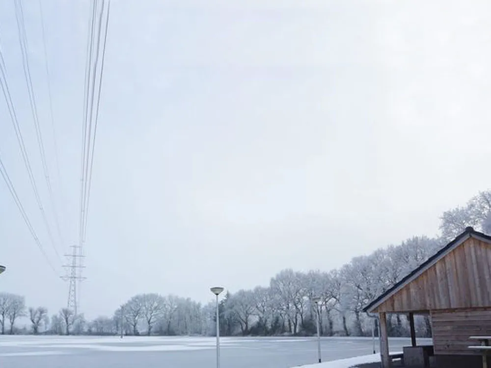 The frozen field of the Sietsenveen rink in winter, with the timber-roofed shelter at the right and a row of frosted trees behind. — IJsbaan Sietsenveen