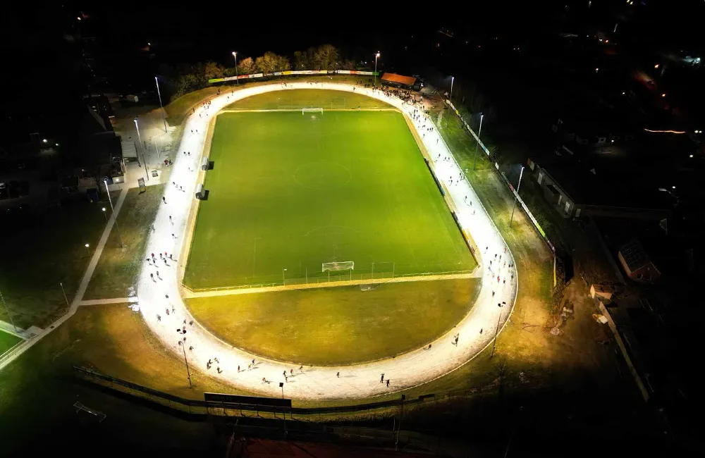 Night aerial view of the lit oval track at Sportpark Veenoord, with the ice edge glowing round the green field in the middle. — IJsbaan Veenoord