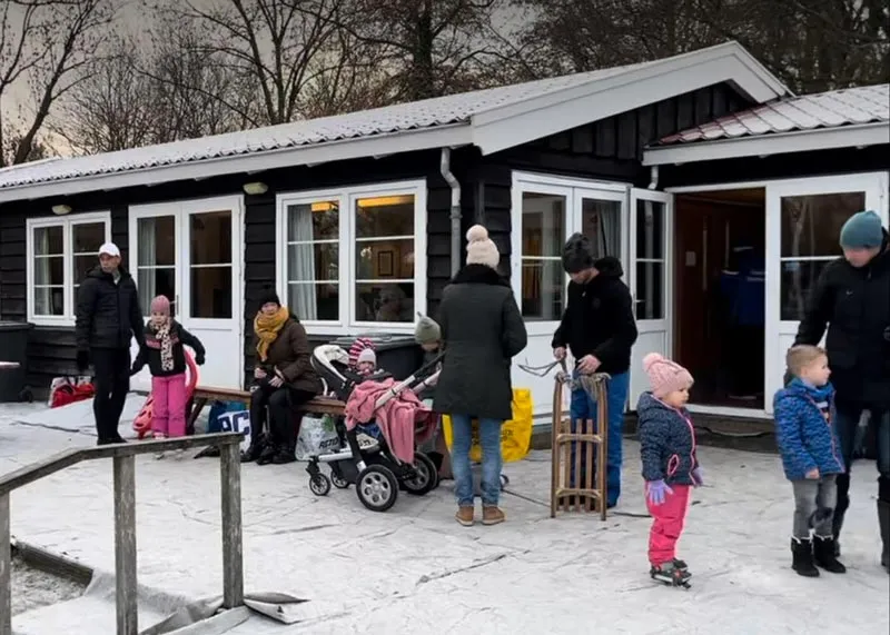 The dark wooden Bamestra clubhouse on a winter evening, with families gathered at its terrace beside the ice. — IJsbaan Bamestra (Middenbeemster)
