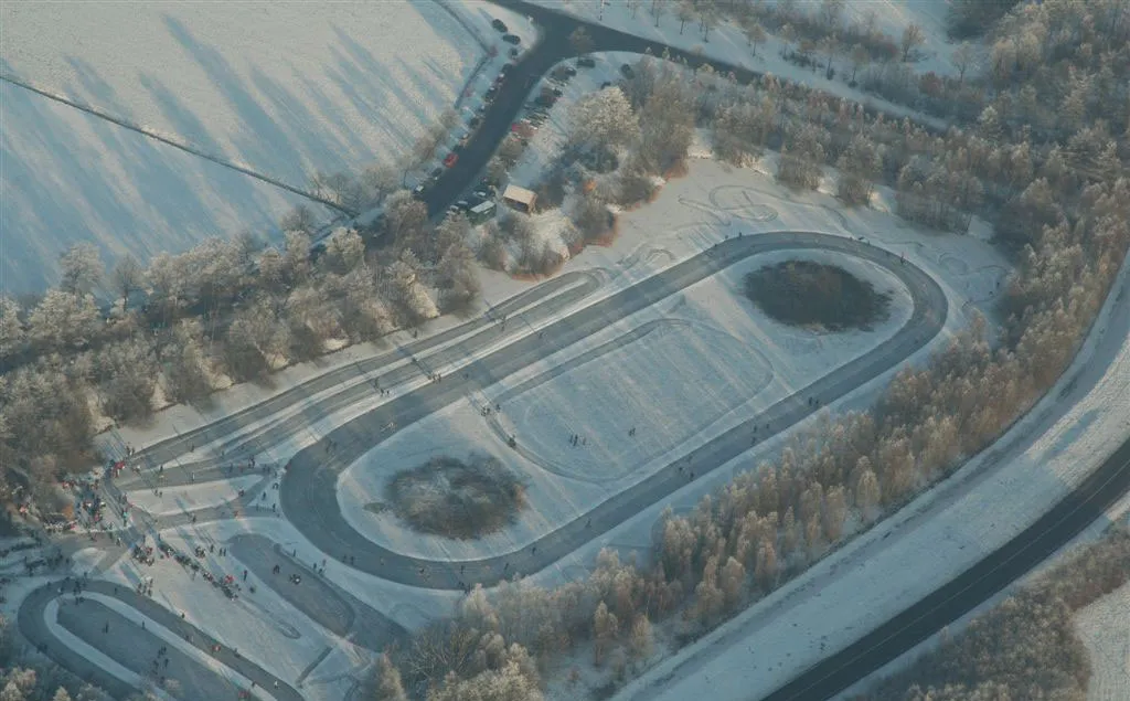 Luchtfoto van de schaatsvijver van Lonneker en de baan in de winter, omringd door bomen en besneeuwde velden. – IJsclub Lonneker