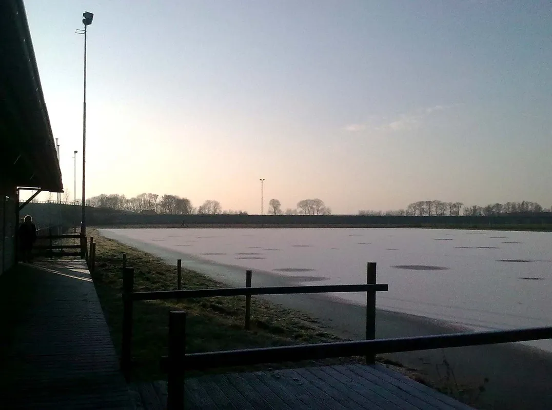 Evening light over the flat, frozen TOG rink with the clubhouse edge at the left. — IJsclub TOG Kampen