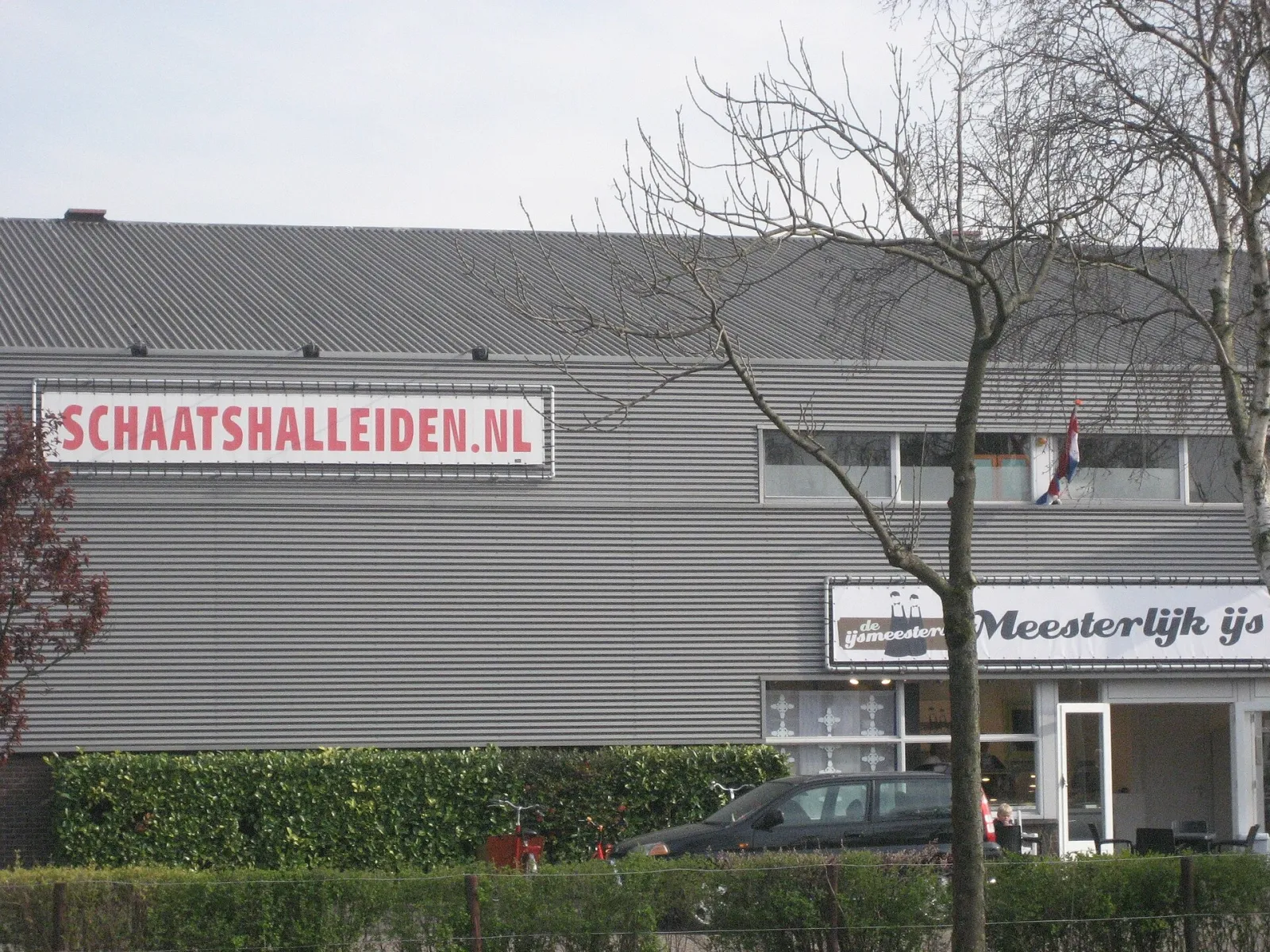 The grey-clad front of the De Vliet skating hall in Leiden with the Schaatshalleiden.nl sign and the ijs lettering over the entrance. — IJshal De Vliet