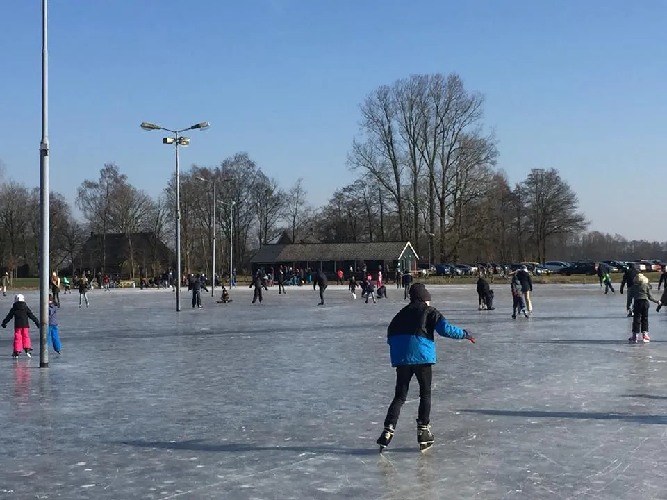 Schaatsers op de bevroren baan van Anreep onder lichtmasten, met de ijskeet en kale bomen op de achtergrond. – IJsvereniging Anreep-Schieven