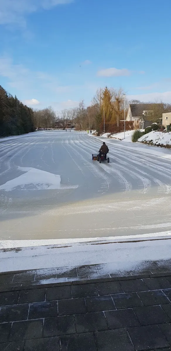 A frozen Hamar rink at Stadskanaal with white tracks cut in the ice and one person on a sled far along the surface. — IJsbaan Hamar (IJsvereniging Hamar, Stadskanaal)