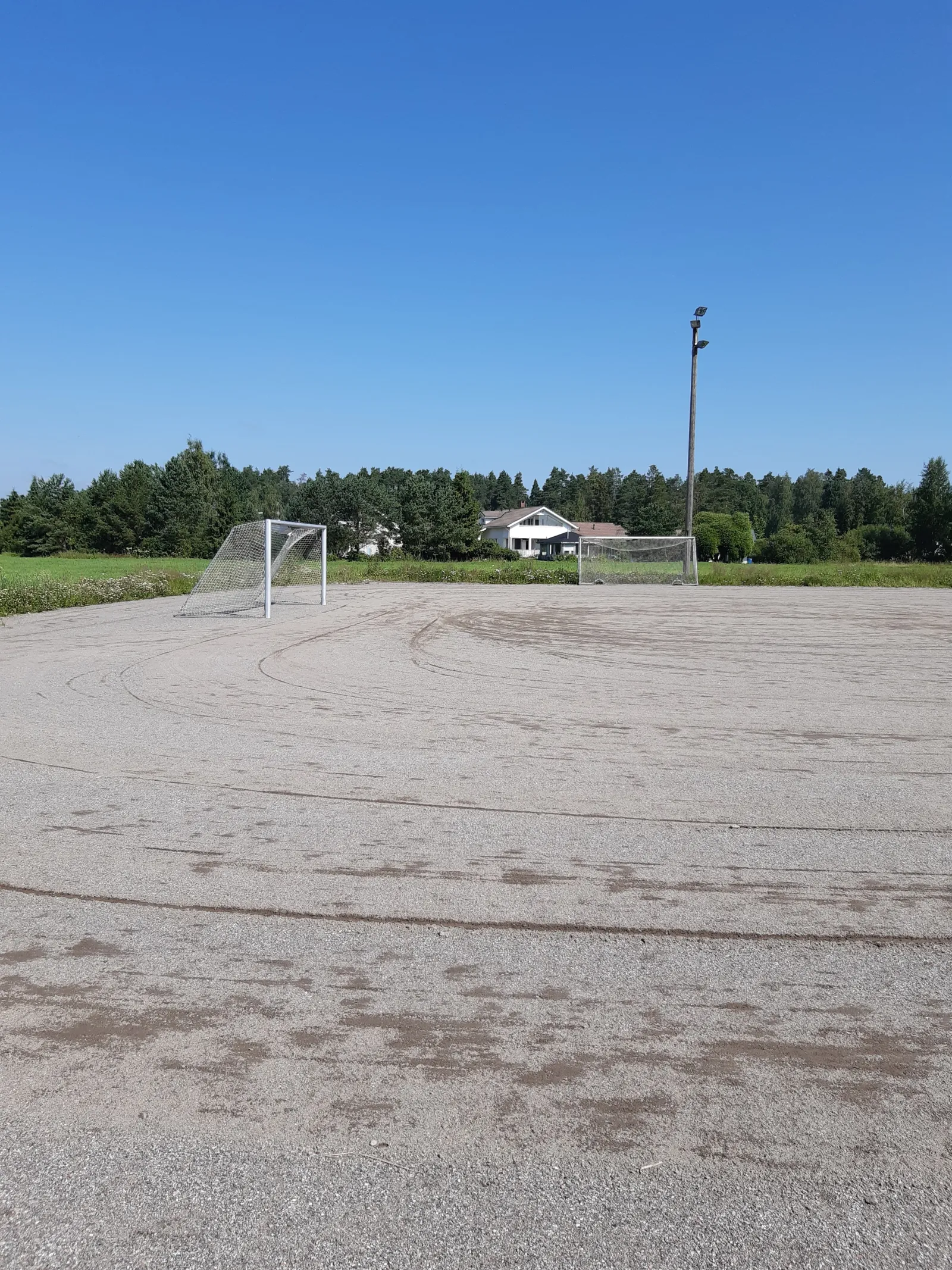 The Ilmestyspäivänpuiston field in summer, a ball field with a gravel (stone-dust) surface with goals; the City of Turku freezes its fields into skating fields in winter. — Ilmestyspäivänpuiston luistelukenttä