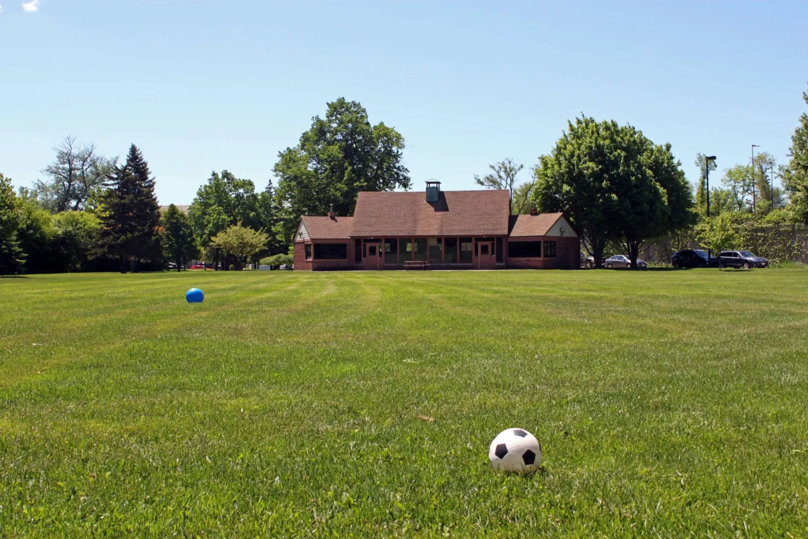 El refugio de Indian Hill Park, en Winnetka, una casa baja de ladrillo con tejado rojo detrás de un amplio césped y árboles frondosos. — Indian Hill Park Outdoor Ice Rink