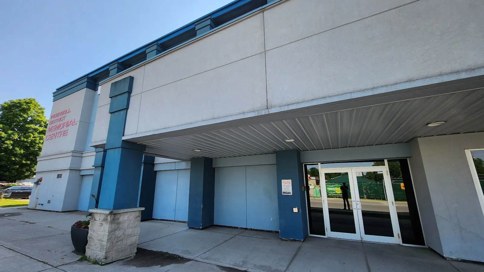 La entrada techada del Ingersoll District Memorial Centre, un edificio gris y azul con su nombre en el muro de la esquina — Ingersoll District Memorial Centre