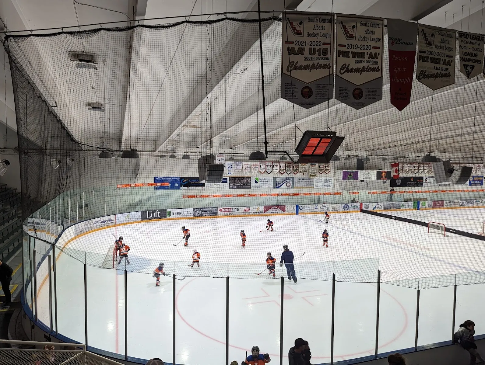 Young skaters spread across the ice at the Taber arena, with the glass, sponsor boards and championship banners above the stands. — Inter Pipeline Community Centre Arenas