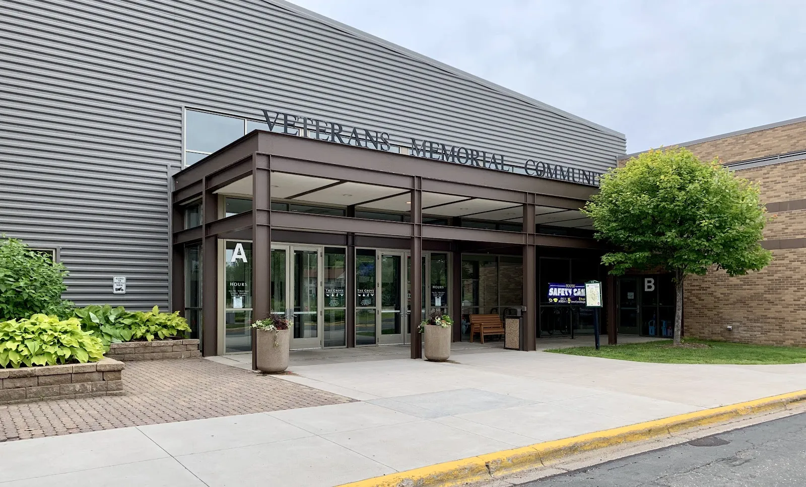 La entrada techada del Veterans Memorial Community Center en Inver Grove Heights, con el nombre a lo largo del muro de metal gris sobre las puertas — Veterans Memorial Community Center Ice Arenas