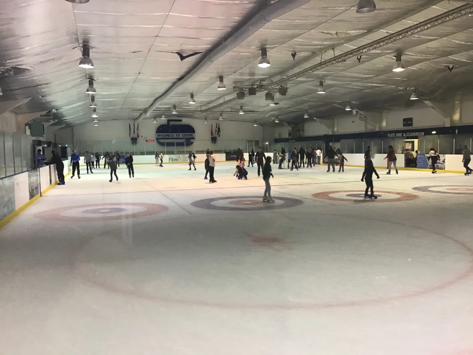 The ice during a public session, looking down the sheet with the centre's curling rings painted on the ice and skaters in the distance. — Inverness Ice Centre