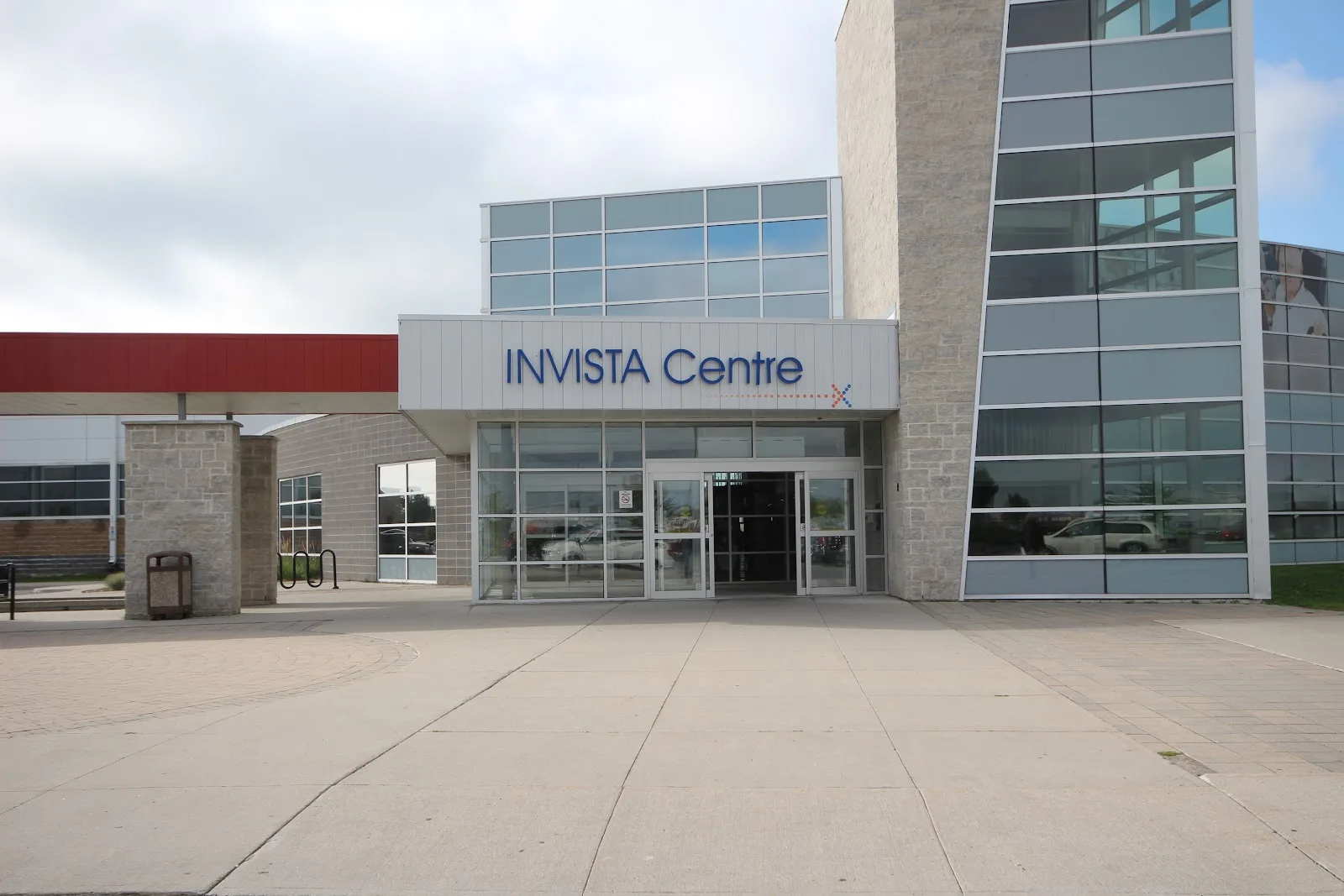 The glass-and-stone main entrance with the INVISTA Centre sign over the doors and a red canopy running off to the left. — INVISTA Centre