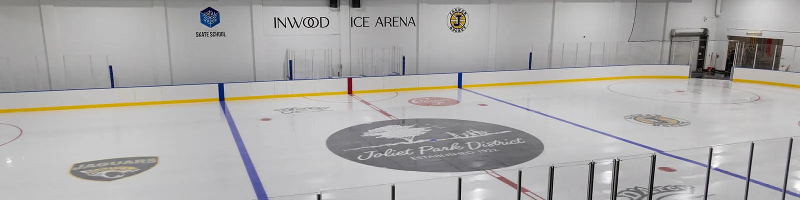 Full ice sheet at Inwood Ice Arena, with "INWOOD ICE ARENA" wall signage and the Joliet Park District logo painted at center ice. — Inwood Ice Arena