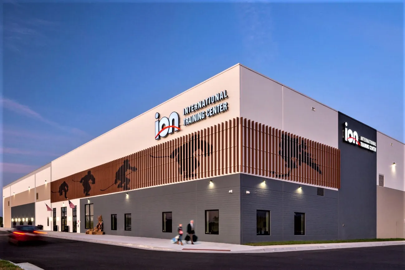 Corner view of the building at dusk with large ION INTERNATIONAL TRAINING CENTER wall signage on two sides and skater silhouette panels, two people walking near the entrance — Ion International Training Center (Leesburg)