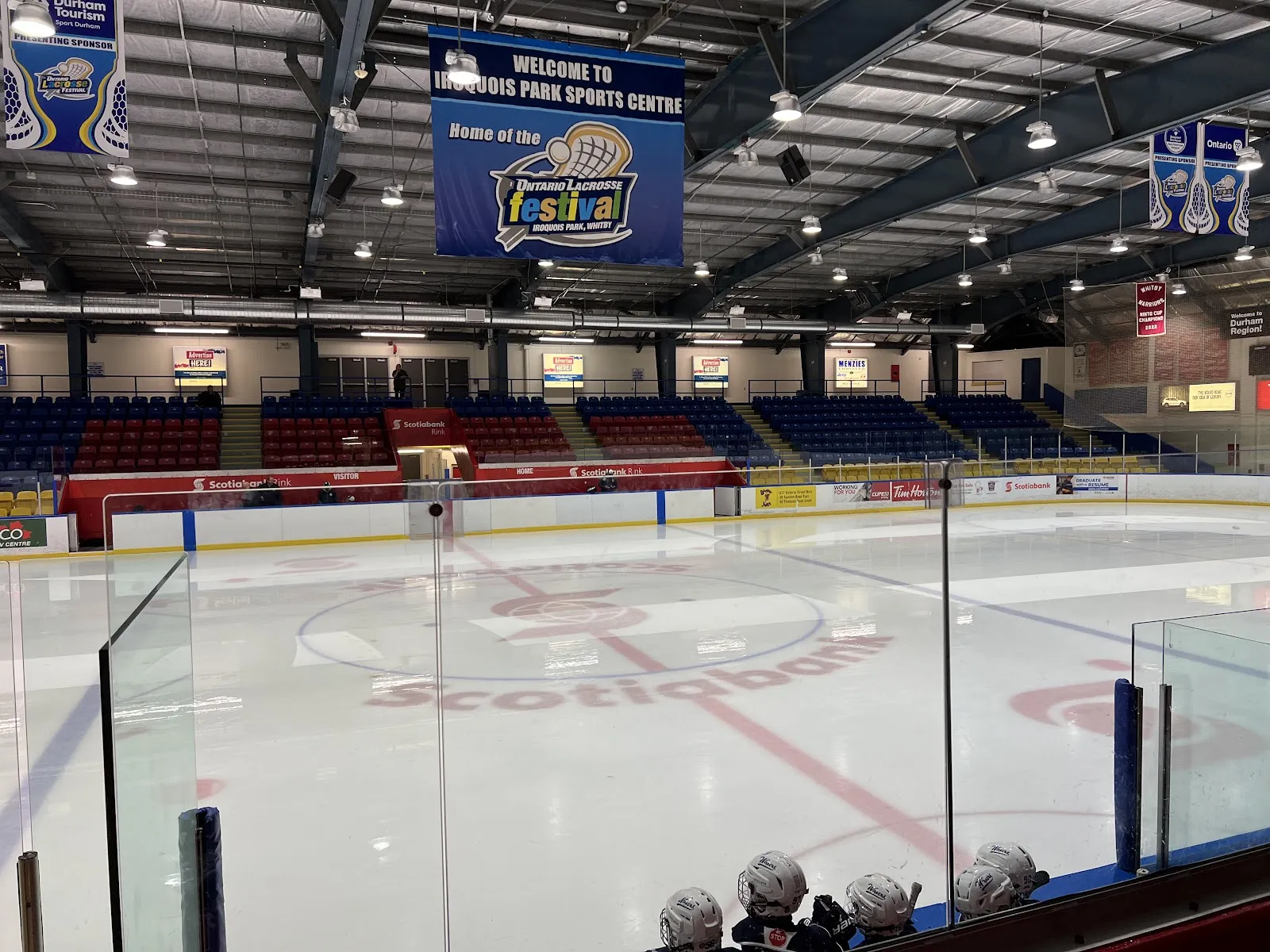 El hielo con la marca Scotiabank de Iroquois Park Sports Centre visto a través del cristal, con asientos rojos y azules y una manta del festival de lacrosse arriba — Iroquois Park Sports Centre