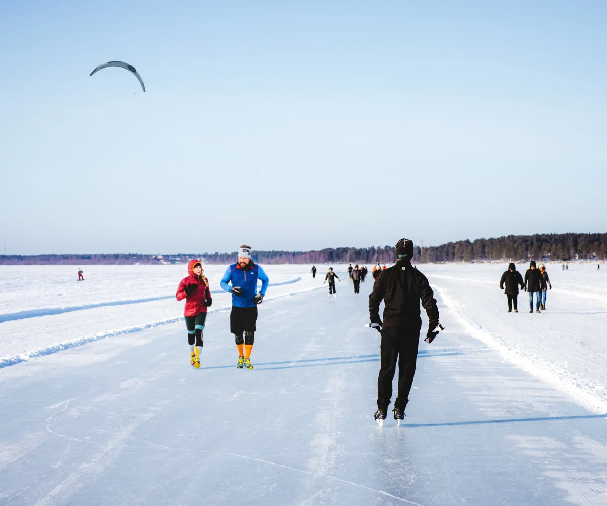 Skridskoåkare som glider längs Isbanan på havsisen vid Luleå en klar vinterdag, med en drake på himlen. – Isbanan runt Luleå centrum