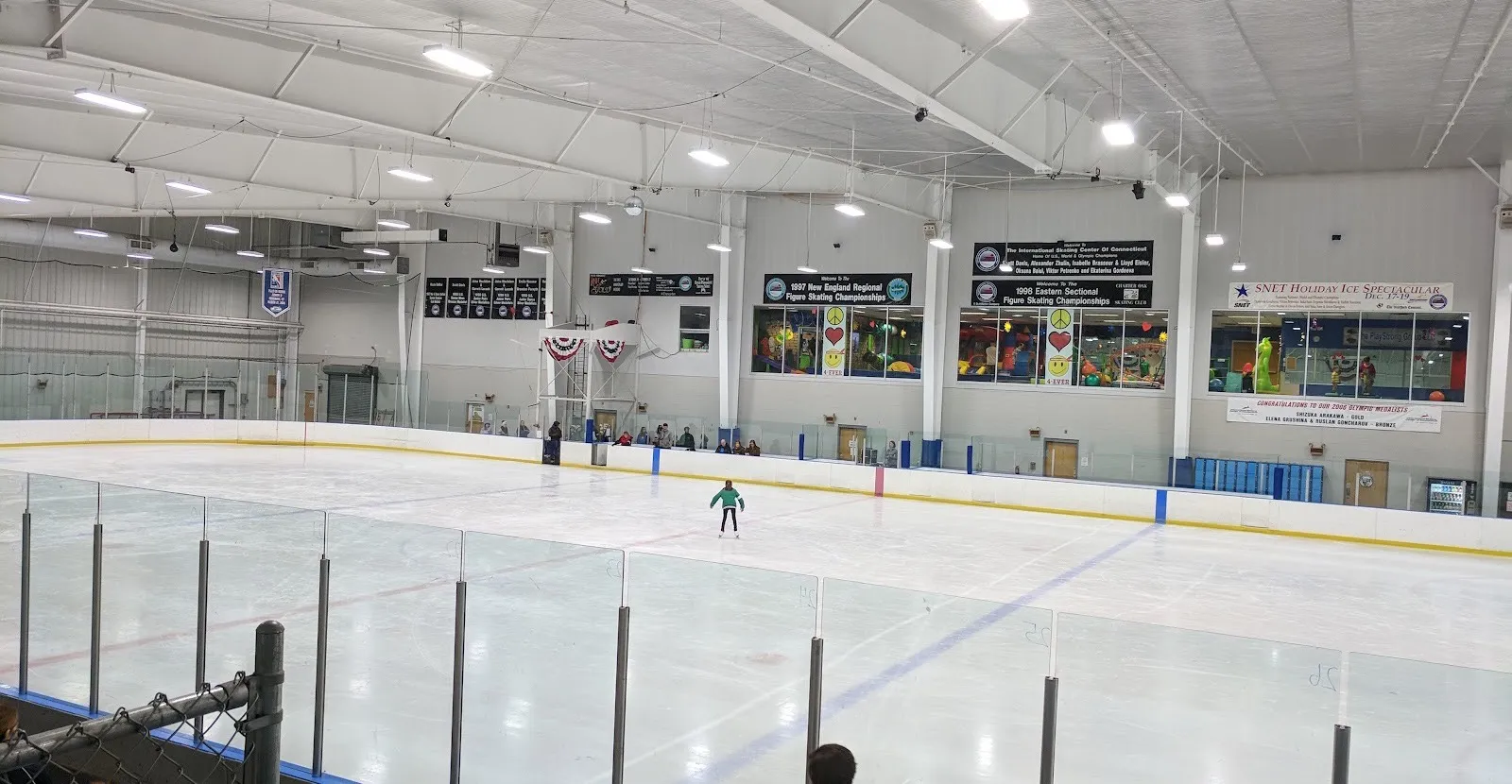 Una pista del International Skating Center of Connecticut desde las gradas, con un patinador practicando bajo mantas de campeonatos — International Skating Center of Connecticut