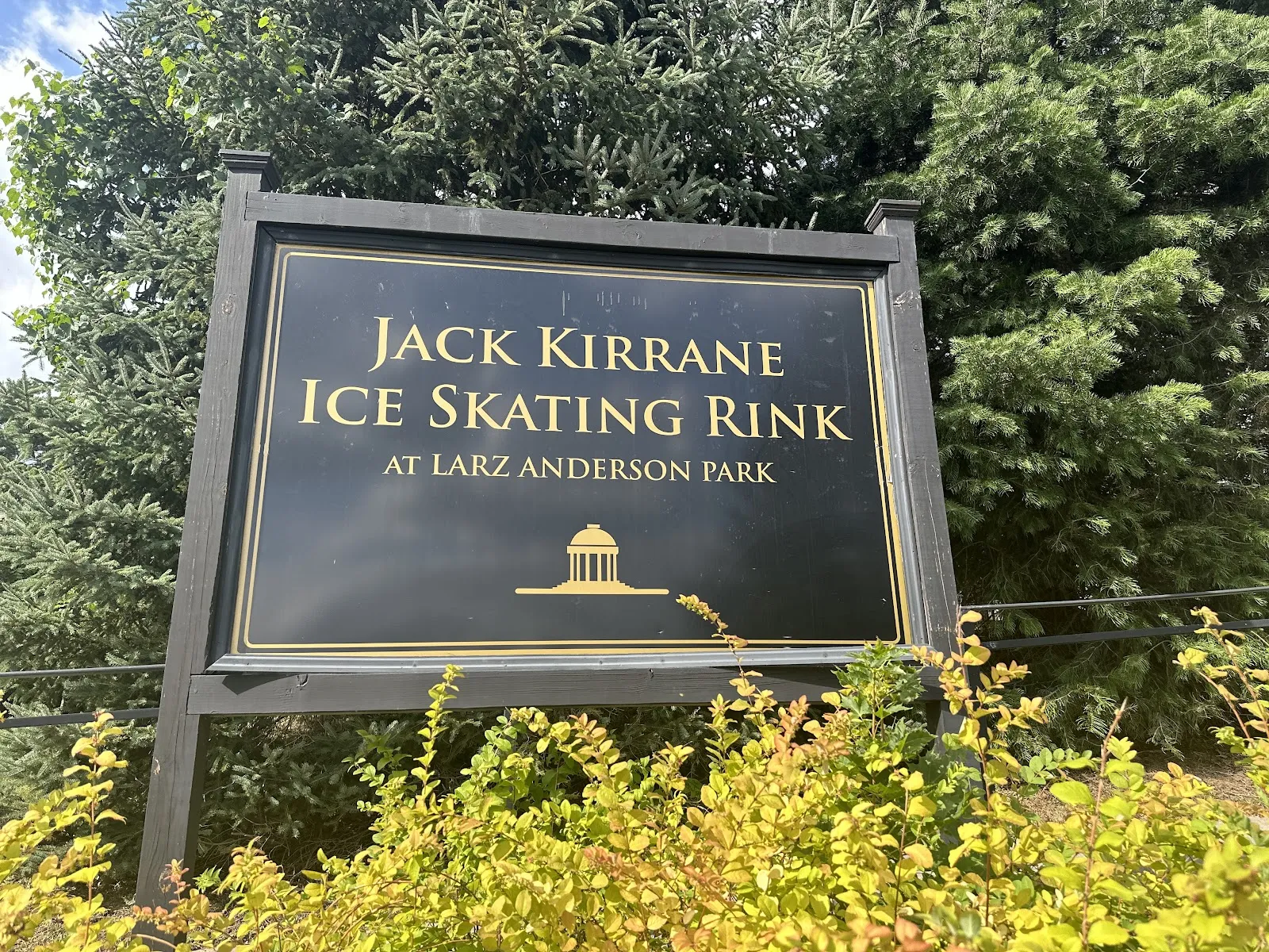 The dark Jack Kirrane Ice Skating Rink entrance sign among shrubs beside the Larz Anderson Park drive. — Jack Kirrane Ice Skating Rink