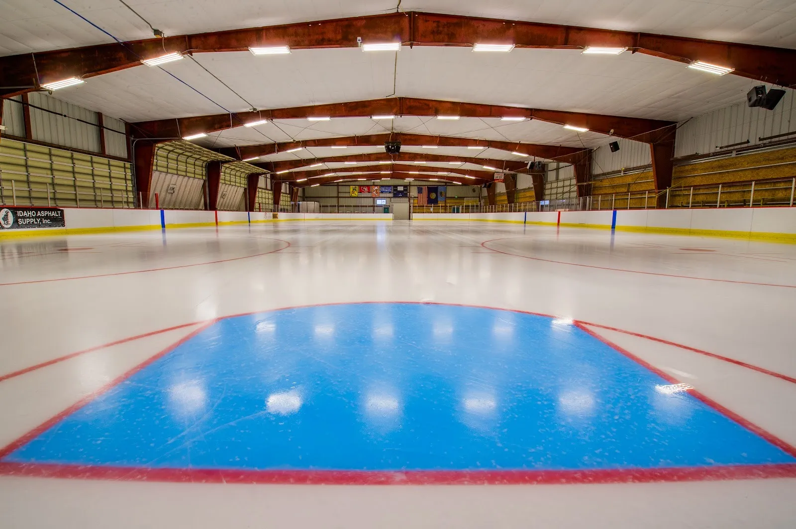 Fresh empty ice at the Joe Marmo / Wayne Lehto rink, a blue crease in front and red steel roof beams over the full sheet — Joe Marmo / Wayne Lehto Ice Arena