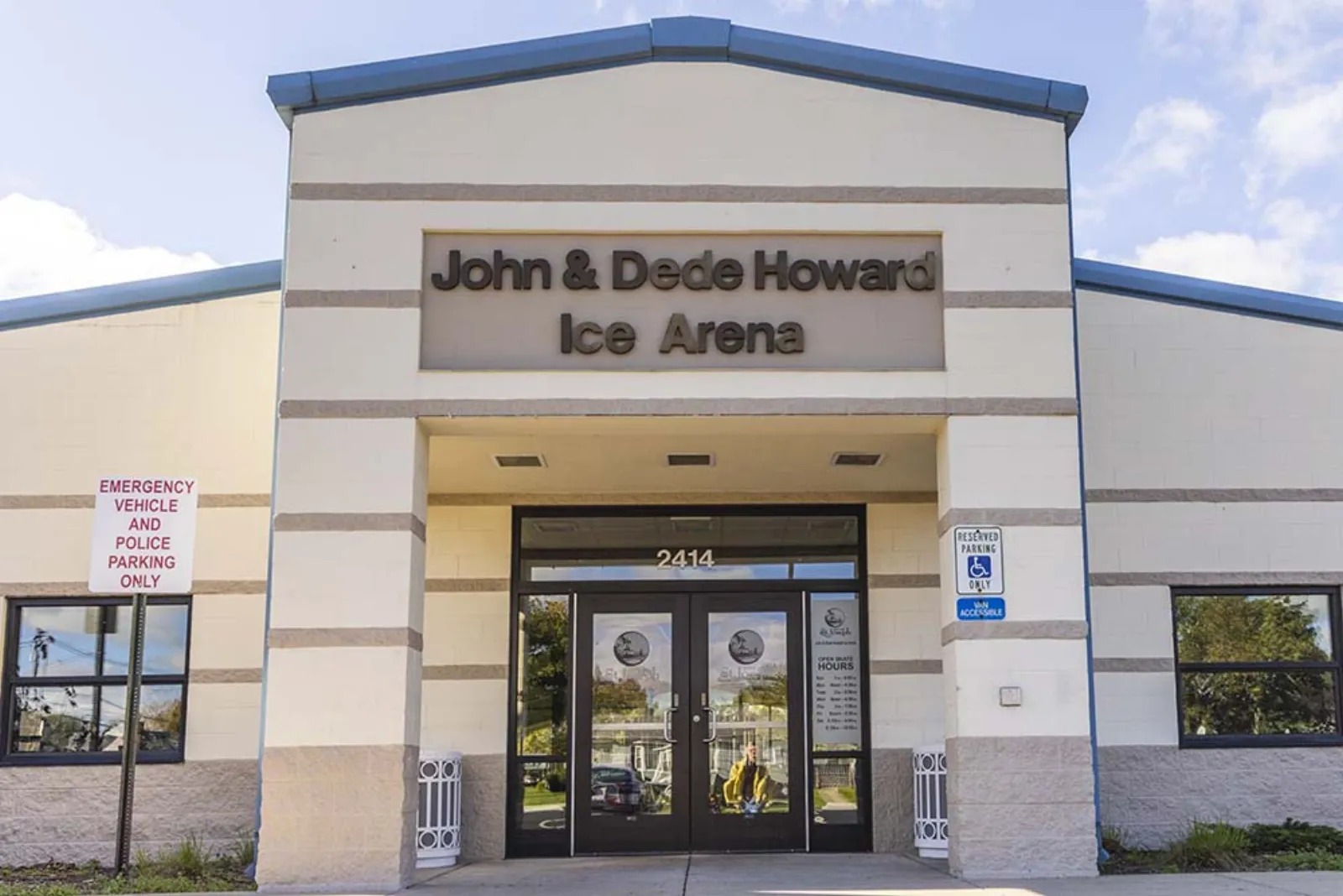 The cream-colored entrance of the John & Dede Howard Ice Arena with its sign over the double doors. — John & Dede Howard Ice Arena