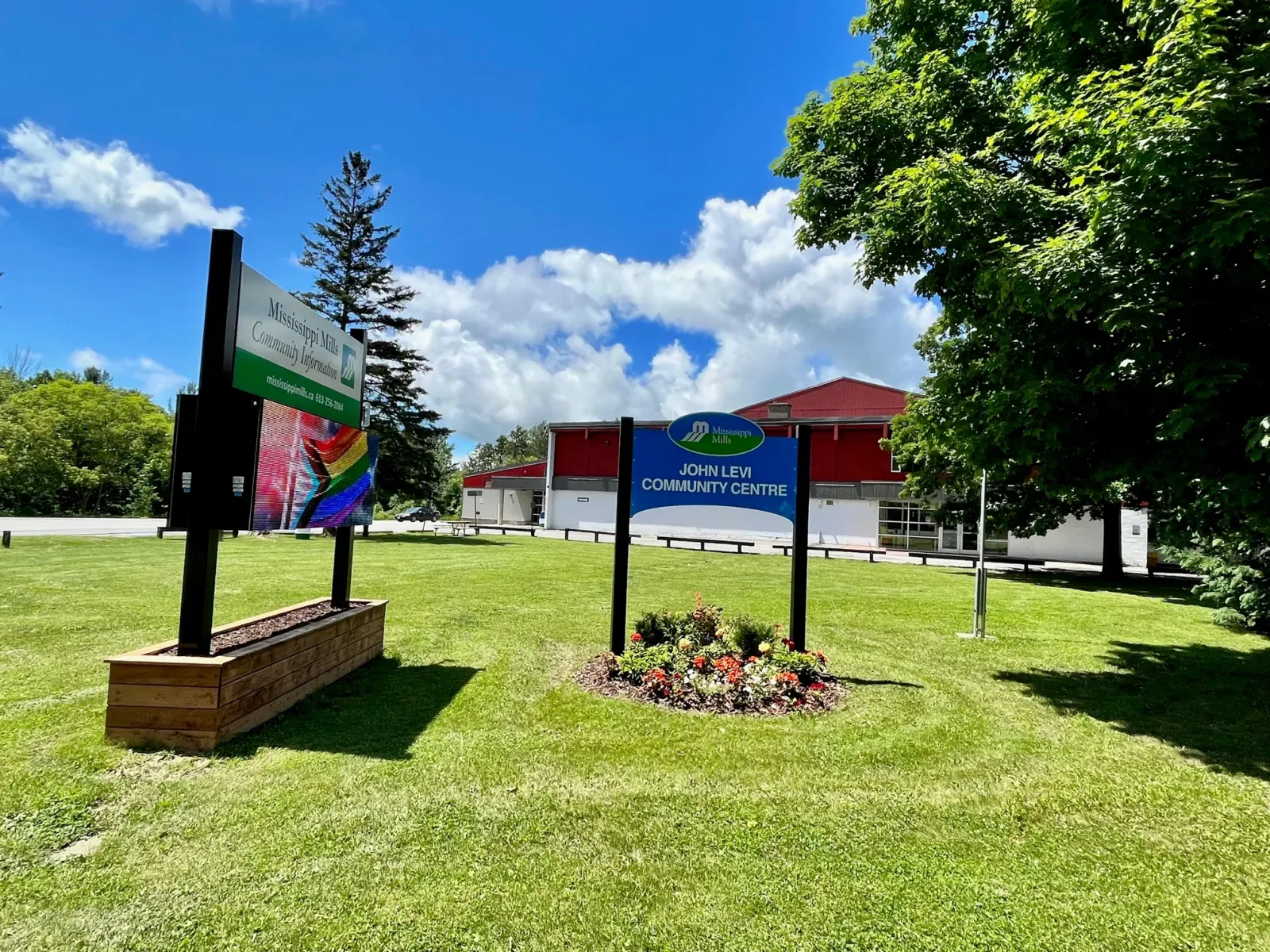 The John Levi Community Centre sign on the lawn, with the red-roofed arena behind it. — John Levi Community Centre (Almonte)